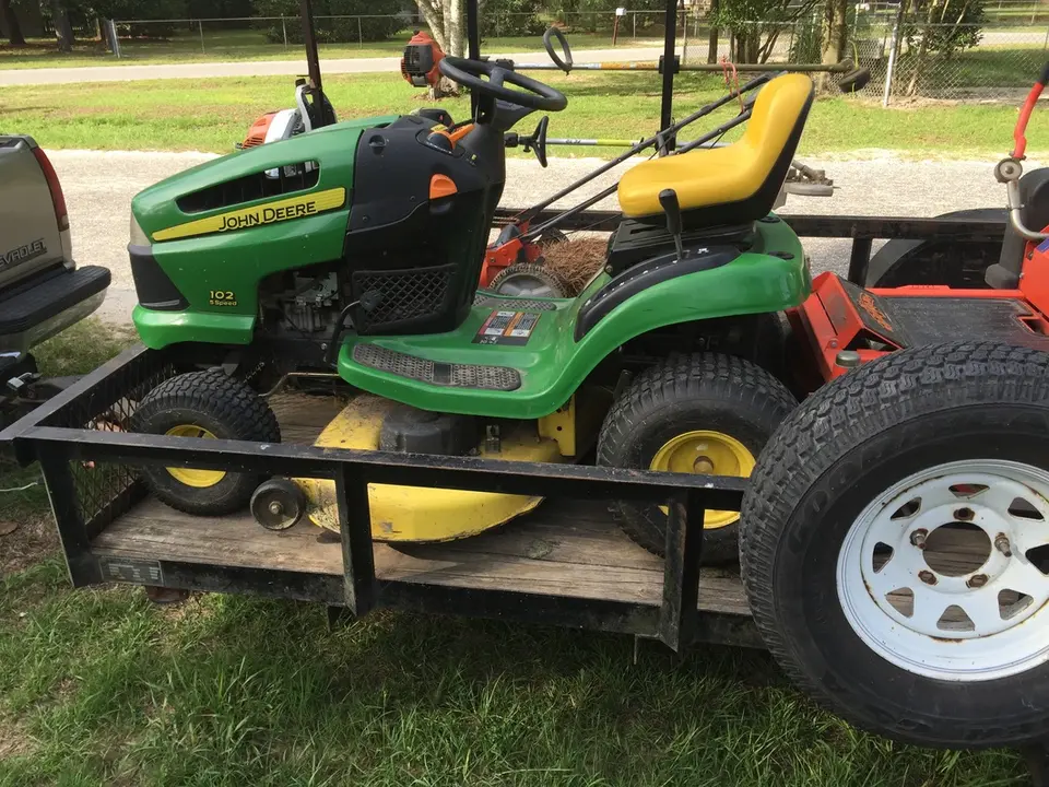 Green riding mower on a utility trailer